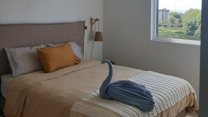 Un dormitorio con cama, ventana y vistas a zonas verdes y edificios.