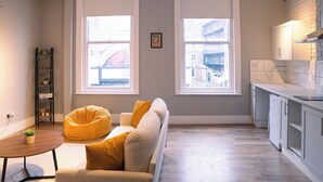 Ein modernes Wohnzimmer mit einer Couch, einem Sitzsack und einem kleinen Tisch. Große Fenster bieten Blick auf Gebäude.