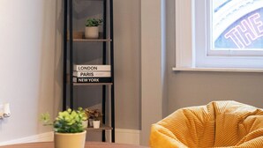 Eine Ecke eines Zimmers mit einem hohen, schwarzen Bücherregal, einem gelben Sitzsack und einem Fenster mit Blick auf ein Gebäude.