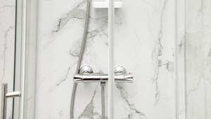 Ein modernes Badezimmer mit einer gläsernen Duschkabine, Marmorwänden und einem Chrom-Duschkopf.
