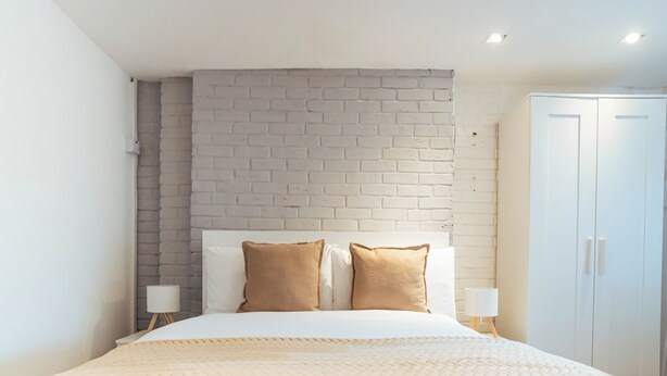 Ein Hotelzimmer mit einem Bett, einer weißen Ziegelwand, zwei Nachttischen mit Lampen und einem Kleiderschrank.