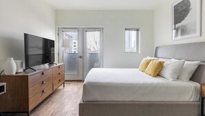 Une chambre à coucher avec un lit, un téléviseur posé sur une commode et une porte donnant sur un espace extérieur.