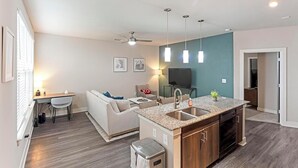 Eine moderne Küche mit Granit Arbeitsplatte, Edelstahlspüle und eingebautem Backofen. Es gibt einen Essbereich mit Tisch und Stühlen sowie ein Wohnzimmer mit Sofa und Fernseher.