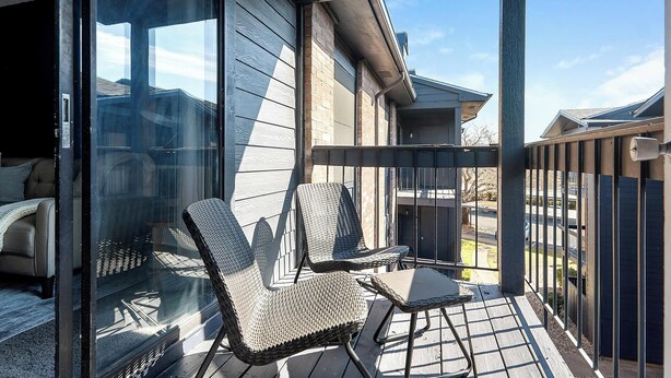Een balkon met rieten stoelen en een kleine tafel, met uitzicht op een woonwijk.