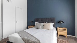 Een slaapkamer met een bed, twee nachtkastjes, een deur en een muur in donkerblauw.