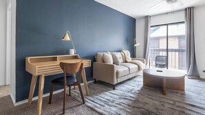 Een moderne woonkamer met een donkerblauwe accentmuur, een houten bureau, een beige bank en een ronde salontafel.