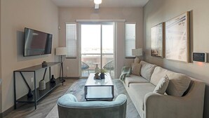 Een moderne woonkamer met een flatscreen televisie, een bank, een salontafel en een balkon met tuinmeubilair.