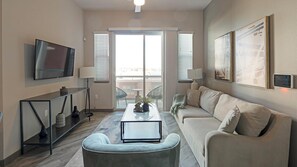A modern living room with a flat-screen TV, a sofa, a coffee table, and a balcony with outdoor furniture. - Landing | Beautiful 2BD, Pool, Clubhouse (Las Vegas)