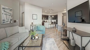 Een moderne woonkamer met een bank, salontafel en een televisie. Er is een keukenhoek met een eettafel en stoelen.