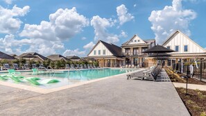 Un área de piscina con sillas de descanso, piscina y un edificio con techo a dos aguas.