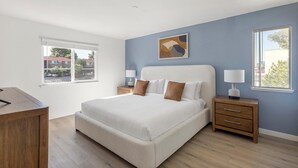 Een slaapkamer met een groot bed, twee nachtkastjes, een bureau en een raam met uitzicht op gebouwen.