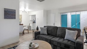 Een moderne woonkamer met een grijze bank, een ronde salontafel en een eethoek op de achtergrond.