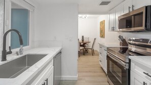 Een moderne keuken met een grote spoelbak, roestvrijstalen apparatuur, en een eethoek met een tafel en stoelen.