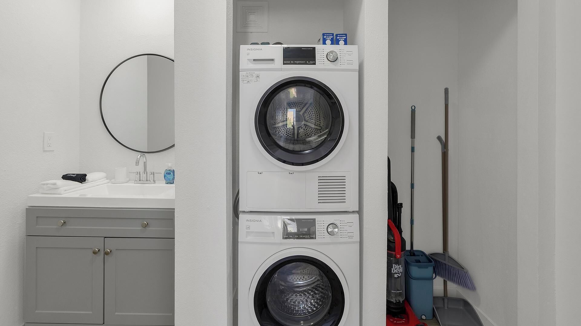 A laundry area with a washing machine and dryer, a sink with toiletries, and a mop and broom.