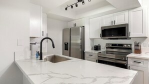 Una cocina moderna con armarios blancos, un refrigerador de acero inoxidable, un microondas y un horno.