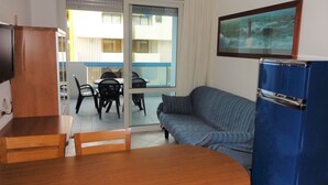 Ein Zimmer mit Esstisch, Stühlen, einer Couch, einem blauen Schrank und einer Glastür, die auf einen Außenbereich mit einem Balkon führt.