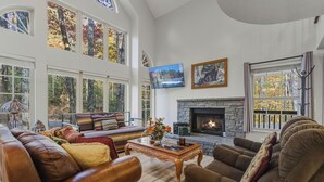 Amplia sala de estar con sofás de cuero, chimenea de piedra, ventanas amplias y un televisor.