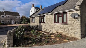 A stone house with solar panels on the roof, a satellite dish, and a garden with stepping stones. - Arum (Portland)
