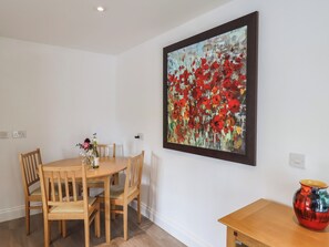 Ein Essbereich mit Holztisch und -stühlen, einer Vase mit Blumen und einem Bild mit roten Blumen an der Wand.
