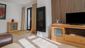 A modern living room with a large flat-screen TV, wooden entertainment unit, and a cozy seating area. - Arum (Portland)