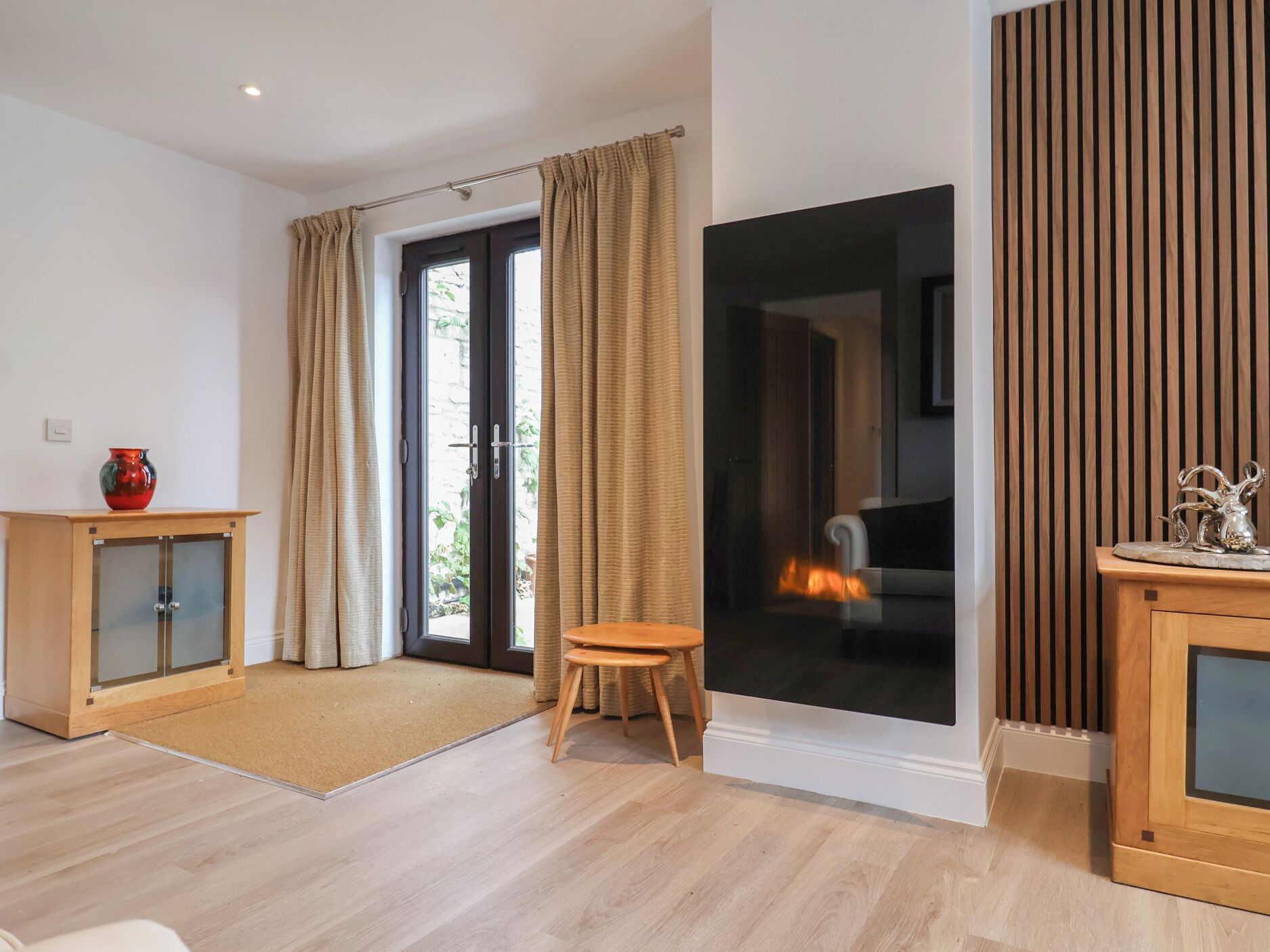 Una sala de estar moderna con un ventanal corredera que da a un balcón, un mueble de madera con un jarrón y un taburete pequeño.