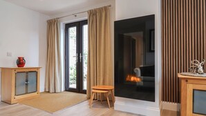 A modern living room with a sliding glass door leading to a balcony, a wooden cabinet with a vase, and a small stool. - Arum (Portland)
