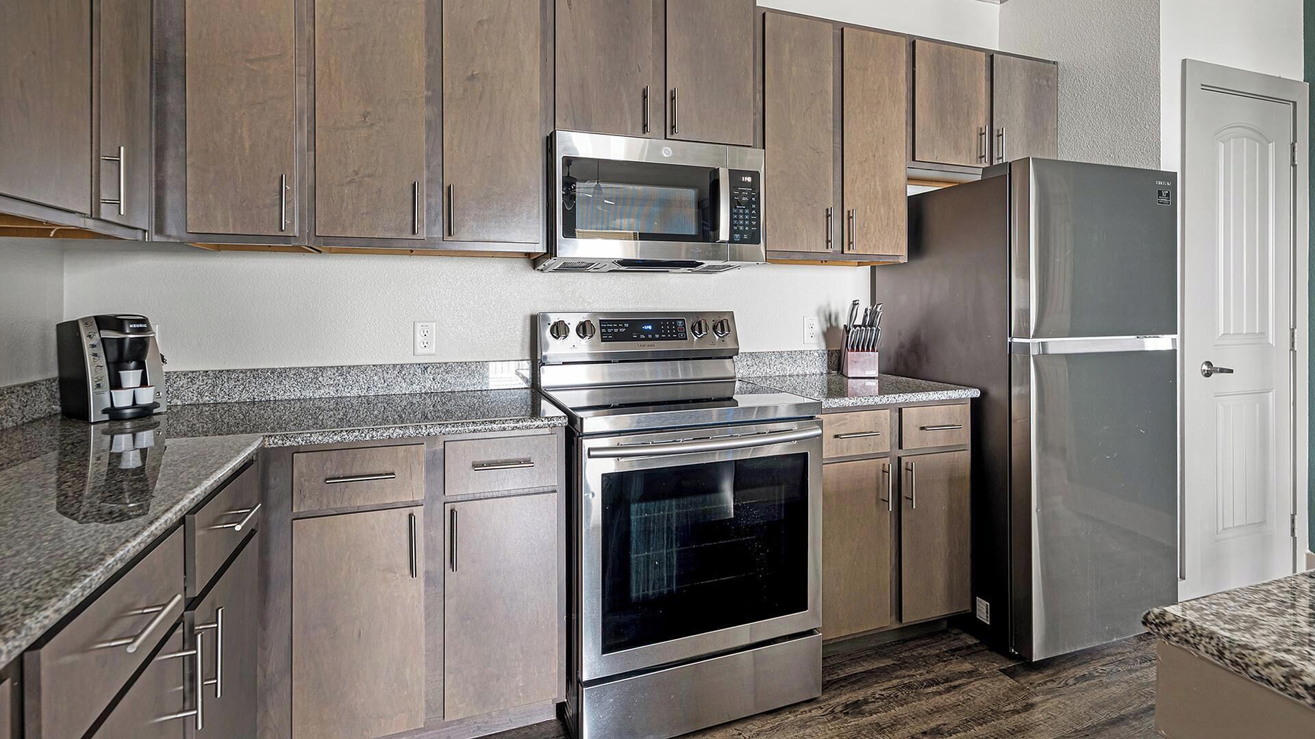 A modern kitchen with stainless steel appliances, wooden cabinets, and granite countertops.