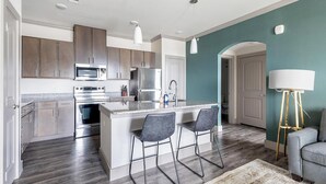 A modern kitchen with a central island, stainless steel appliances, and bar stools. - Landing | Amazing 1BD, Clubhouse, Gym (Manor)