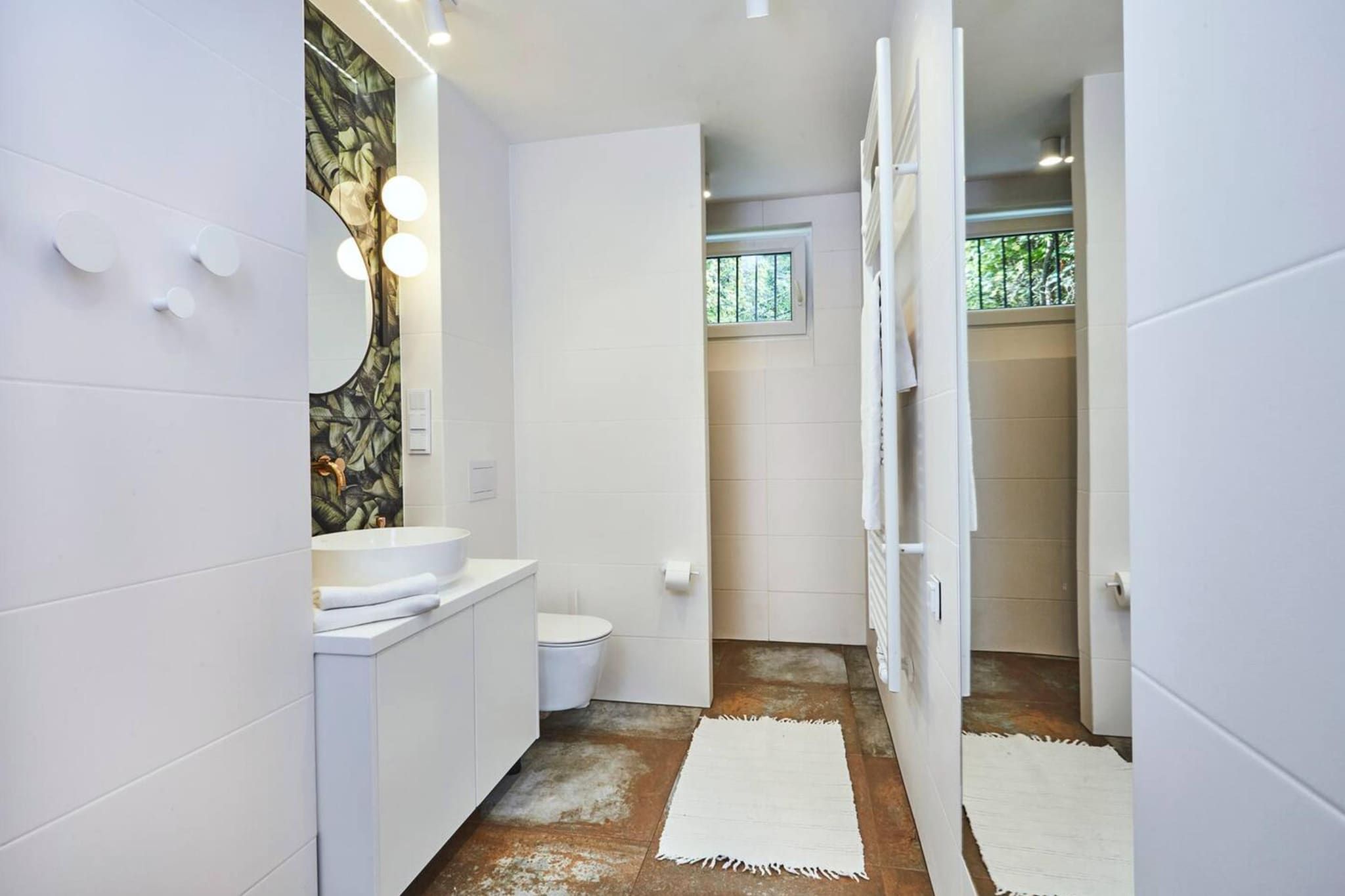 Un baño moderno con lavamanos, inodoro y zona de ducha blancos.