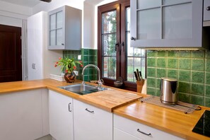 Cocina moderna con armarios blancos, encimera de madera, pileta de acero inoxidable y salpicadero con azulejos verdes.