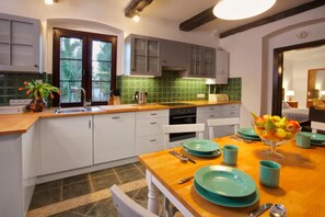 A modern kitchen with white cabinets, a green tiled backsplash, and a wooden dining table set with teal plates and fruit. - Comfortable holiday home, pool, sauna, jacuzzi (Sasino)