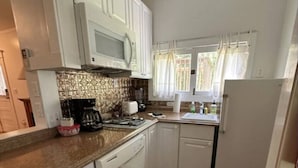 Una cucina compatta con mobili bianchi, un forno a microonde, una moka e un lavandino.