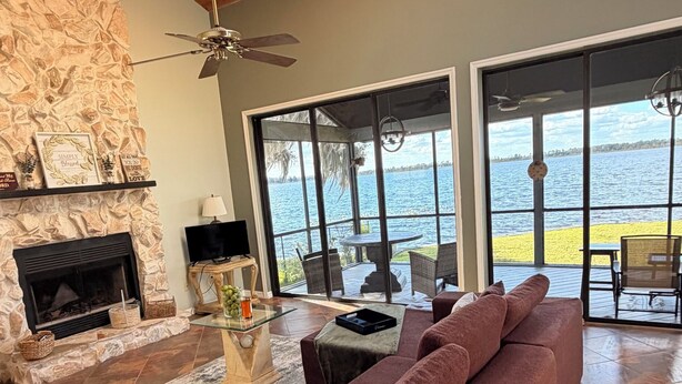 Ein geräumiges Wohnzimmer mit Kamin aus Stein, einem großen Sofa und Blick auf das Wasser.