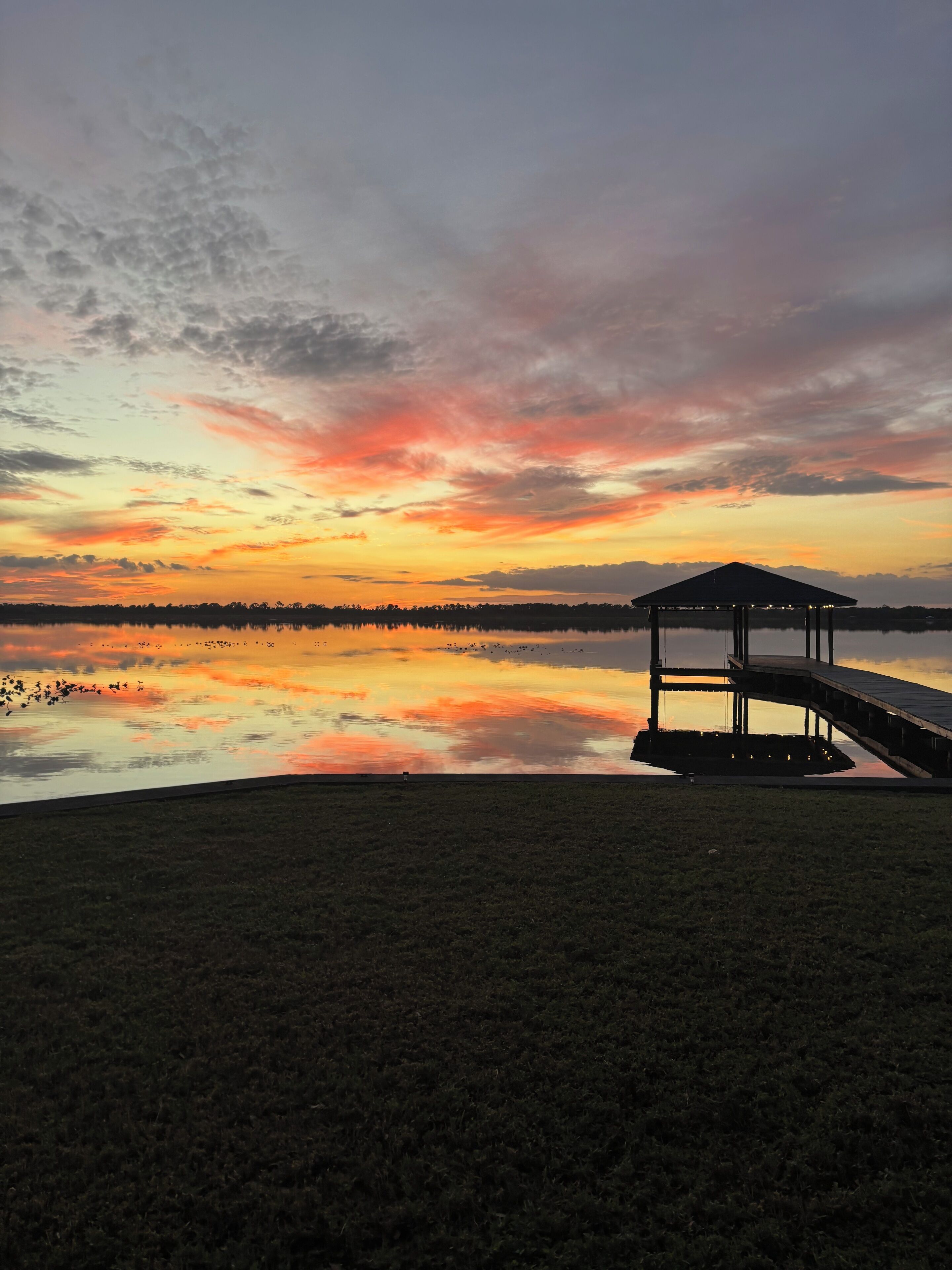Um gazebo à beira de um lago calmo ao pôr do sol.