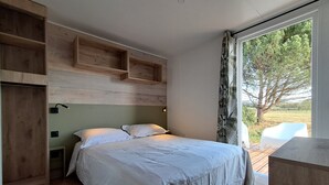 A bedroom with a bed, wooden shelves, a nightstand, and a window with a view of trees. - Suite Hôtel (Le Temple-sur-Lot)