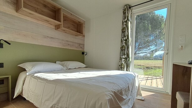 A bedroom with a bed, wooden headboard, and a view of the outdoors through a glass door. - Suite Hôtel (Le Temple-sur-Lot)