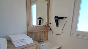 A bathroom with a wooden vanity, a sink, a mirror, and two hair dryers mounted on the wall. - Suite Hôtel (Le Temple-sur-Lot)
