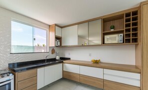 A modern kitchen with a built-in stove, a microwave, and a large window overlooking a beach. - House w/ Grill in Front of the Beach Lbra0011 (Ilhéus)