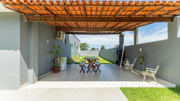 A covered patio with a tiled roof, a table and chairs, and a view of a building in the background. - House w/ Grill in Front of the Beach Lbra0011 (Ilhéus)