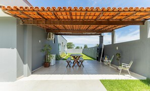 A covered patio with a tiled roof, a table and chairs, and a view of a building in the background. - House w/ Grill in Front of the Beach Lbra0011 (Ilhéus)