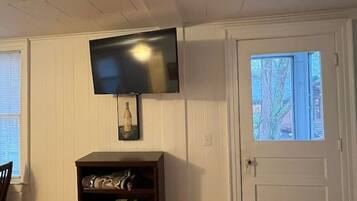 Quarto com televisão de tela plana na parede, uma estante de livros, porta com janela e piso de madeira.