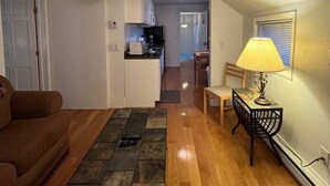 A living room with a sofa, a coffee table, and a dining area with a lamp. - Gulf Stream House - Unit 11 (Hammondsport)