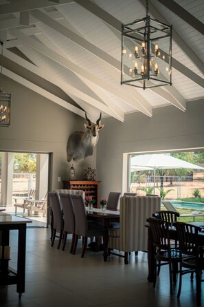 A dining area with a high ceiling, a chandelier, and a mounted animal head sculpture. - Opperman Safari House - All-Inclusive, Exclusive use safari lodge in Namibia (GROOTFONTEIN, NAMIBIA)