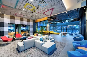Ein moderner Lounge-Bereich mit Ecksofa, roten und blauen Sesseln und einem großen Fenster mit Blick auf die Stadt.