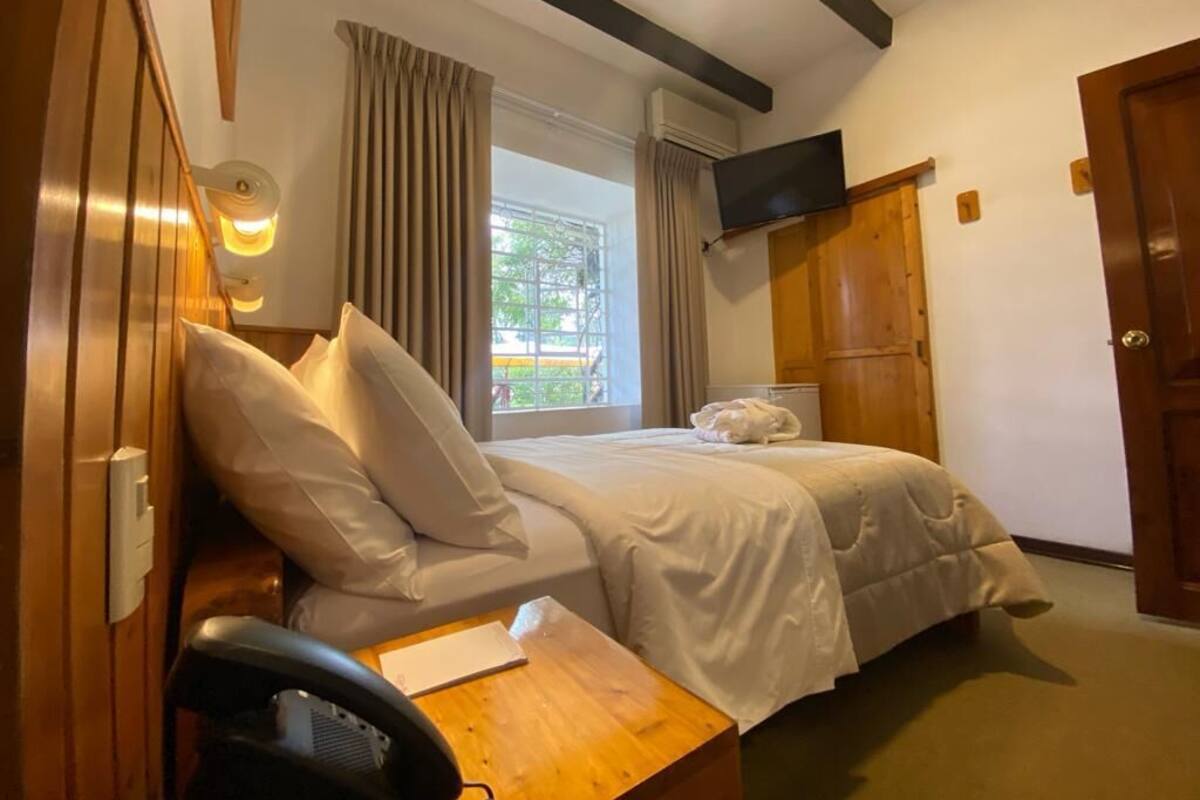 A hotel room with two beds, a desk, a chair, a TV, and a window with curtains.