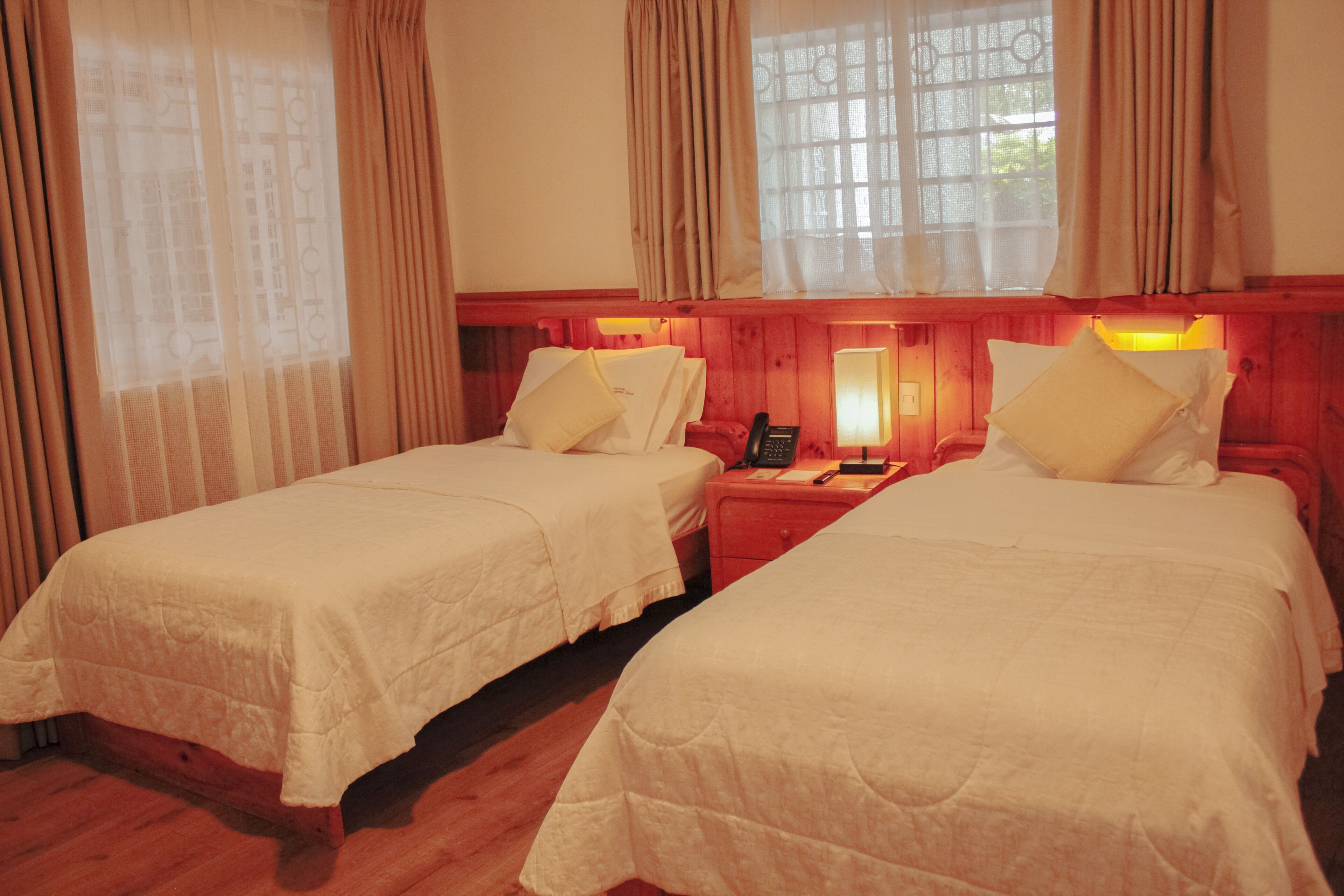 Quarto com duas camas, piso de madeira e janela com cortinas.