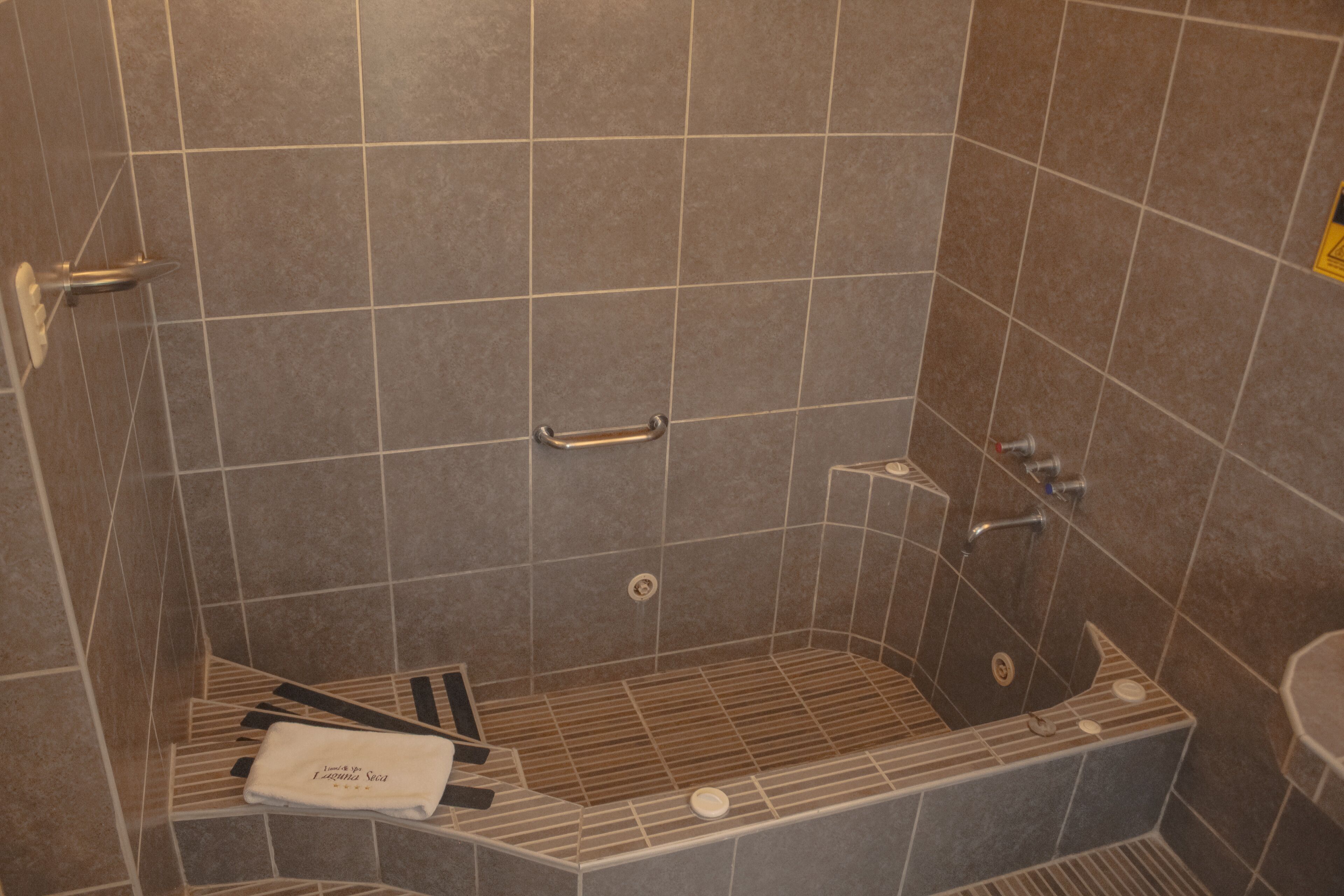 A modern shower area with a built-in bench, a towel rack, and a handheld showerhead.