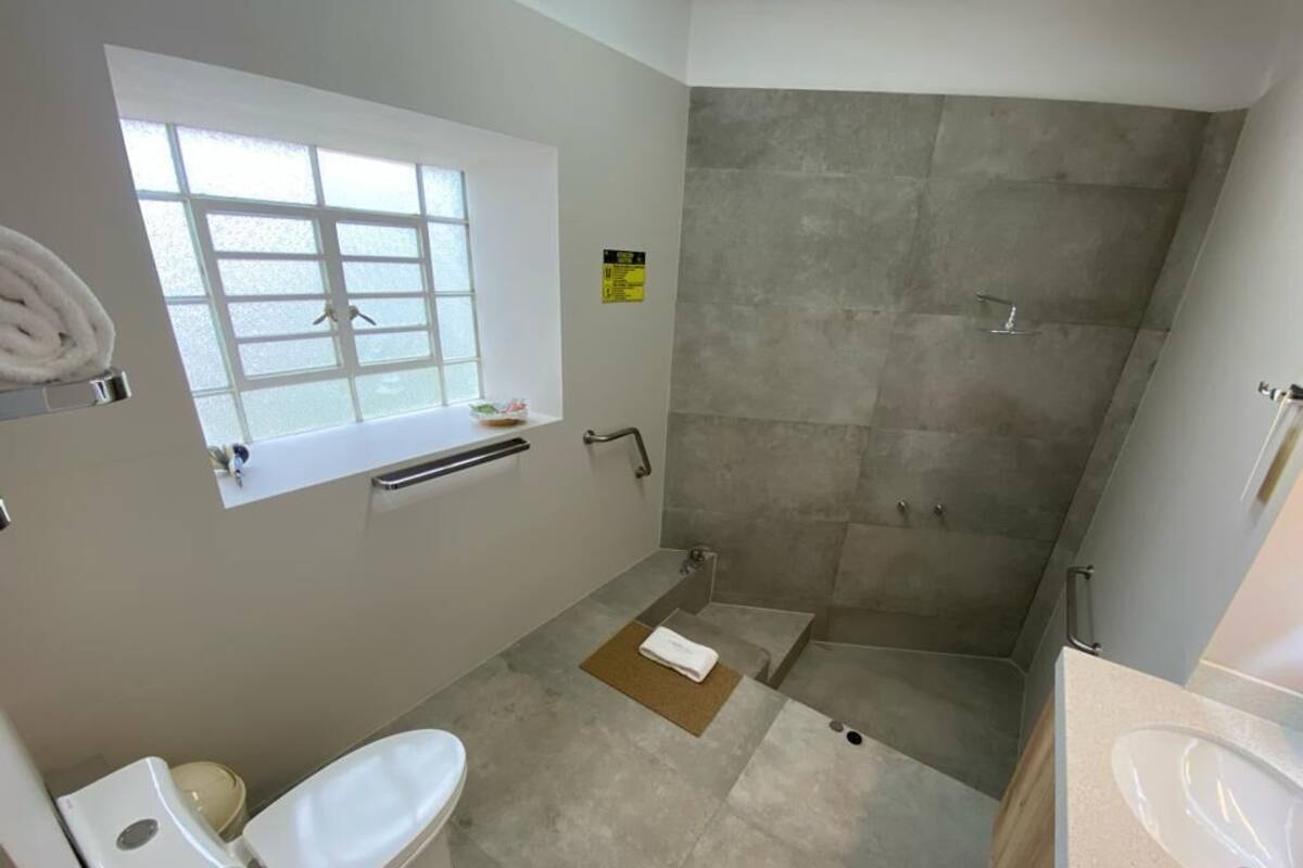 A bathroom with a toilet, sink, shower, and a window.