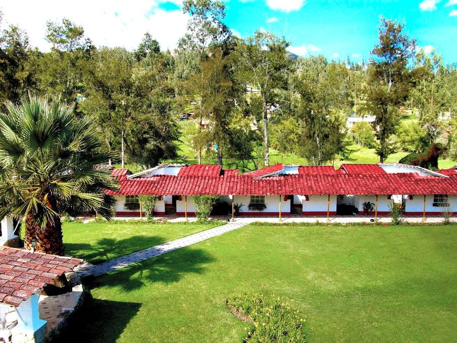 A row of white buildings with red roofs, surrounded by green grass and trees.