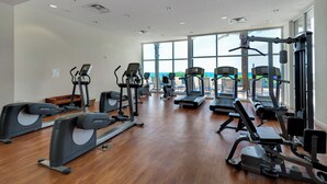 Un gimnasio amplio con diversas máquinas de cardio, estaciones de pesas y un ventanal que ofrece vistas al exterior.
